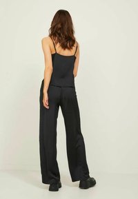 Camisola de satin preta com alças ajustáveis, combinada com calças largas de corte solto e preto. Textura suave e design fluido.