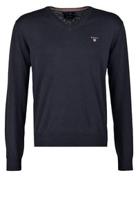 Granatowy sweter w serek, wykonany z miękkiego dzianiny, z długimi rękawami i małym haftowanym logo na piersi. Ściągacze przy rękawach i na dole.