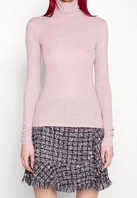 Hellrosa Rollkragenpullover aus strukturiertem Strickmaterial mit langen Ärmeln. Kombination mit einem schwarz-weißen karierten Rock mit Fransen.