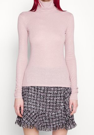 Light pink turtleneck sweater made of textured knit fabric, featuring long sleeves. Paired with a black and white fringed plaid skirt.