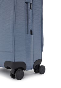 Modrá softshellová kufřík vyrobená z texturované tkaniny, se boční kapsou, uzávěrem na zip a čtyřmi černými koly pro snadnou mobilitu.