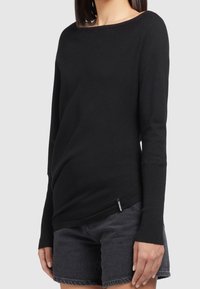 Pull noir à manches longues avec un large décolleté, des poignets côtelés et une texture douce. Associé à un short en denim foncé.