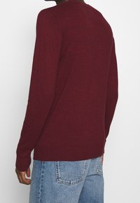 Burgundy stickad tröja med långa ärmar, rund halsringning och ribbad nederkant. Mjuk textur och kroppsnära design, vy från baksidan.