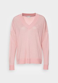 Pull à col en V rose clair à manches longues avec poignets et ourlet côtelés, arborant un logo "TH" subtil sur le côté gauche de la poitrine.