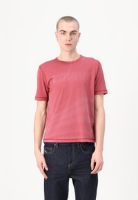 Rød T-skjorte med korte ermer og rund hals, med en subtil logo-trykk. Stoffet ser glatt ut med en lett glans.