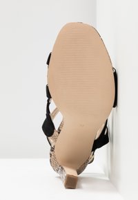 Vue de la semelle d'une sandale à talons hauts pour femmes avec une semelle texturée beige, des brides noires et un talon et des côtés à motif serpent, taille 37.