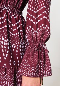 Bordeaux mønstrede bluse med hvide geometriske designs, med elastiske manchetter og en samlet talje for en flydende silhuet.