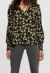 Svart blus med gult blommönster. Har V-ringning och långa, samlade ärmar med elastiska manschetter. Slät tygtextur.