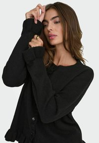 Cardigan noir en maille avec un col arrondi, des manches longues et des poignets côtelés. Dispose d'une fermeture à boutons sur le devant et d'une texture douce.