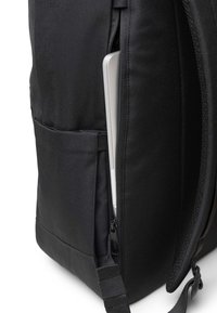 Mochila de tela negra con cremallera lateral. Cuenta con un bolsillo que contiene un portátil plateado. Textura suave y correas de hombro ajustables.