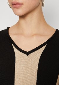 Czarny i beżowy sweter dzianinowy z dekoltem w serek, ozdobiony szerokim pionowym wzorem w paski. Teksturowany materiał z prążkowanym wykończeniem.