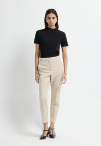 Zwarte hoge hals t-shirt gecombineerd met beigekleurige broek met een nette pasvorm. Schoenen zijn zwart met enkelbandjes. Eenvoudig ontwerp, soepel materiaal, slim fit.
