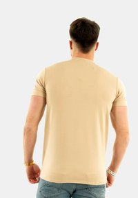 Camiseta de manga corta beige con escote redondo, diseño ajustado y textura suave. El modelo lleva unos vaqueros de color azul claro.