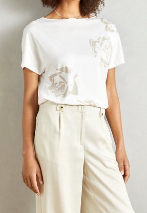 Biała koszulka z beżowym wzorem róż, krótki rękaw i luźny krój, zestawiona z jasnobeżowymi spodniami z wysokim stanem z dodatkiem guzika.