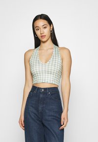 Top cropped em gingham verde e branco com um design de halter neck. O tecido é leve, com um decote em V e uma silhueta ajustada. Combinado com jeans escuros.