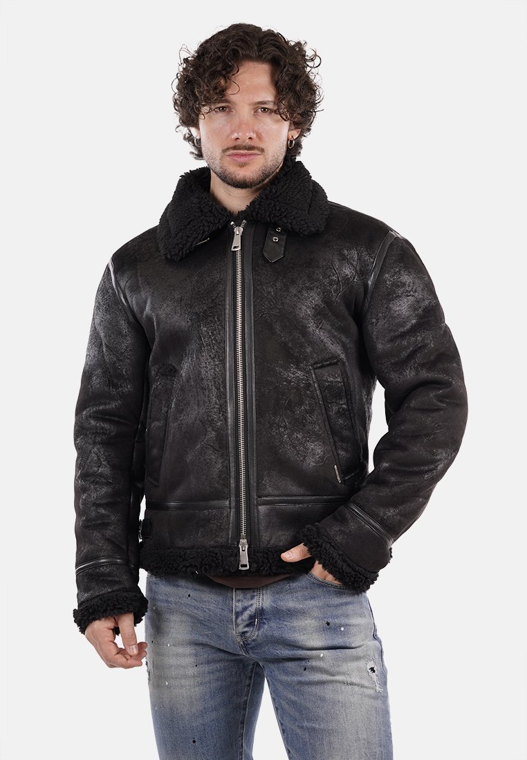 Giacca di pelle nera con colletto e polsini in pelliccia sintetica, chiusura frontale con zip, finitura testurizzata e tasche laterali. Indossata sopra una camicia azzurro chiaro e jeans.