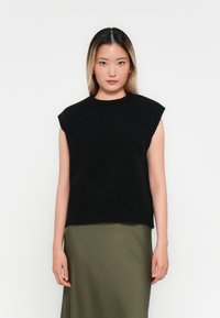 Svart ermeløs strikket topp med rund hals og avslappet passform; kombinert med et langt olivengrønt skjørt. Myk tekstur, minimalistisk design.