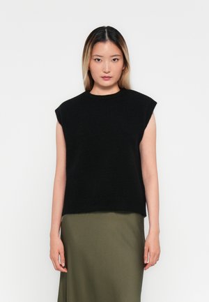 Svart ermeløs strikket topp med rund hals og avslappet passform; kombinert med et langt olivengrønt skjørt. Myk tekstur, minimalistisk design.