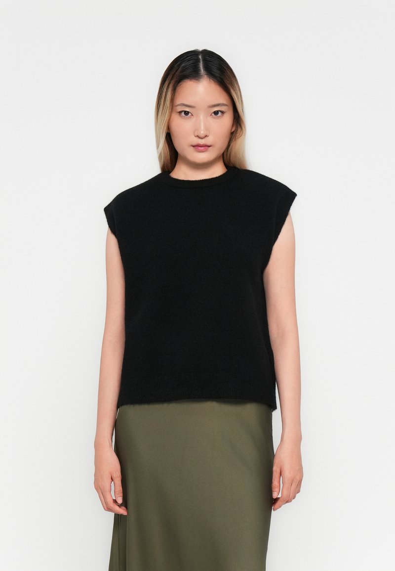 Svart ermeløs strikket topp med rund hals og avslappet passform; kombinert med et langt olivengrønt skjørt. Myk tekstur, minimalistisk design.