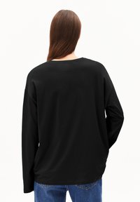 Schwarzes Langarmshirt mit entspannter Passform, Rundhalsausschnitt und weichem Stoff. Kombiniert mit blauen Jeans aus Denim, die ein schlichtes Design zeigen.