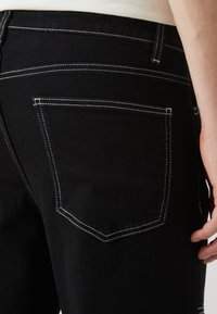 Sorte denim jeans med en tettsittende design, med hvite sømtoner, en baklomme med firkantet form, og en jevn tekstur.