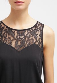 Débardeur noir avec un empiècement en dentelle orné de motifs floraux complexes, texture lisse et encolure arrondie.