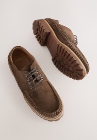 Chaussures en daim marron avec une surface texturée, un design à lacets et des semelles en caoutchouc robustes présentant un motif de bande de roulement pour une meilleure adhérence.