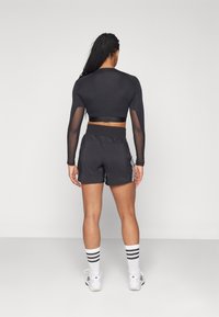Top corto negro de manga larga con mangas de malla, combinado con pantalones cortos deportivos negros que tienen rayas blancas en los laterales. Se lleva con calcetas blancas a rayas.
