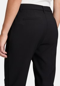 Čierne nohavice na mieru s hladkým materiálom, s jednou zadnou vreckom a jemným prešitím. Strih je štruktúrovaný, čo poskytuje elegantný siluetu.