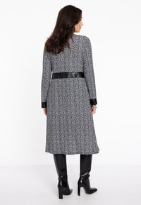 Schwarz-weiß gemustertes Kleid mit tailliertem Schnitt, langen Ärmeln und einem schwarzen Kunstledergürtel. Glatte Textur; knielanges Design.