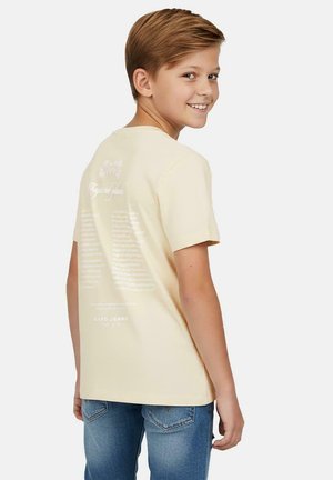 Lichtgele katoenen t-shirt met korte mouwen, met tekstpatronen en merklogo gedrukt op de achterkant. Draagt bij blauwe spijkerbroek.