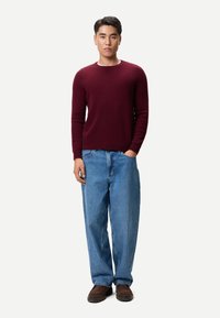 Vinröd stickad tröja med rund halsringning, matchad med ljusblå vida jeans och bruna slip-on skor. Enkel, avslappnad design genomgående.