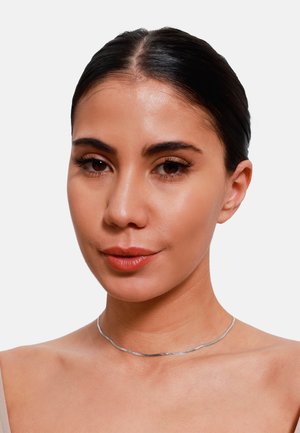 Silberne Choker-Halskette mit wellenförmigem Design, glatter Textur und minimalistischer Ästhetik, getragen an einem nackten Hals vor einem neutralen Hintergrund.