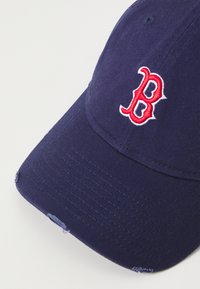 Cappellino da baseball blu navy in twill di cotone, con logo ricamato "B" rosso e bianco, con cuciture visibili e leggermente sfilacciato.