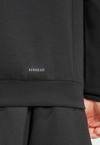 Black Aeroready sweatshirt with a smooth texture. Features a low hem and visible branding in white at the bottom.