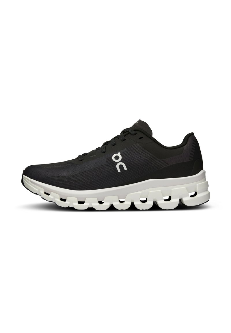 Chaussure de sport noire avec un dessus texturé, semelle intermédiaire blanche dotée d'un design segmenté distinctif, et un logo simple sur le côté.