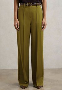Maslinasto zelene široke hlače od glatkog materijala, s prednjim nabranjima i smešnim pojasom s kružnom kopčom.