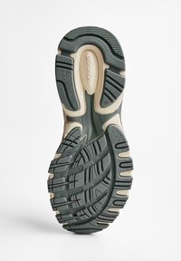Talpa pantofului este realizată dintr-un material de cauciuc verde închis, cu modele texturate și accente bej. Prezintă șanțuri adânci pentru tracțiune și stabilitate.