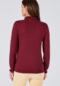 Maglione bordeaux con colletto a coste, motivo a noci di cocco testurizzato e maniche aderenti. L'orlo presenta dettagli a coste per una vestibilità aderente.