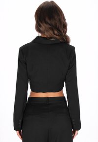 Czarna krótka kurtka z klapami, długimi rękawami i guzikami na mankietach. Gładki materiał z dopasowanym krojem.