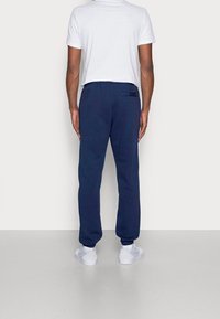 Marinblå mjukisbyxor med elastisk midja och nedhasade anklar, tillverkade av mjukt tyg. Vita sneakers används. Bakvy av outfiten.