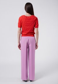 Suéter corto de punto rojo con patrón de olas texturizado, combinado con pantalones de pierna ancha en color rosa pastel de cintura alta.