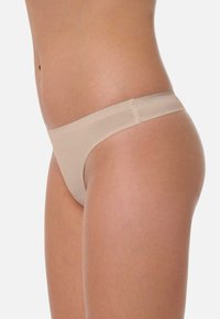 Culotte en thong nude, avec une bande élastique lisse et une couverture minimale, fabriquée à partir d'un tissu doux et transparent avec un design sans couture.