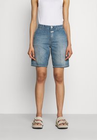 Shorts de mezclilla en azul claro con corte recto, diseño de cinco bolsillos y cierre frontal con botón. Combinados con una camiseta sin mangas blanca y sandalias casuales.