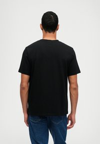 Μαύρο κοντομάνικο T-shirt, φτιαγμένο από μαλακό βαμβάκι με λαιμόκοψη, λεία υφή και άνετη ε φαρμογή. Φορεμένο με μπλε τζιν.