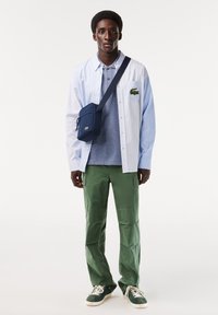 Vit och blårandig skjorta, grå pikétröja, gröna cargobyxor, marinblå axelväska och gröna sneakers med vita sulor.