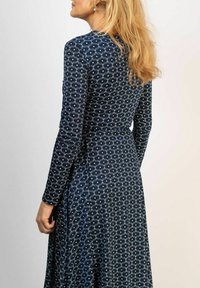 Mörkblå långärmad klänning med vit snurrande mönster. Figursydd överdel, utsvängd kjol och knytband vid midjan. Slät tygtextur.