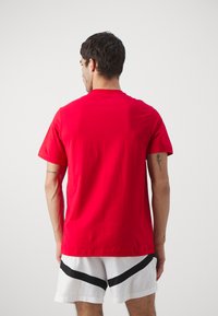 Rød bomulds t-shirt med korte ærmer og rund halsudskæring, vist fra bagsiden. Stoffet fremstår glat uden synlige mønstre eller grafik.