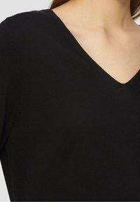 Schwarzer V-Ausschnitt-Pullover aus weichem Strickstoff. Er zeichnet sich durch einen figurbetonten Schnitt, eine glatte Textur und eine saubere Verarbeitung am Ausschnitt aus.