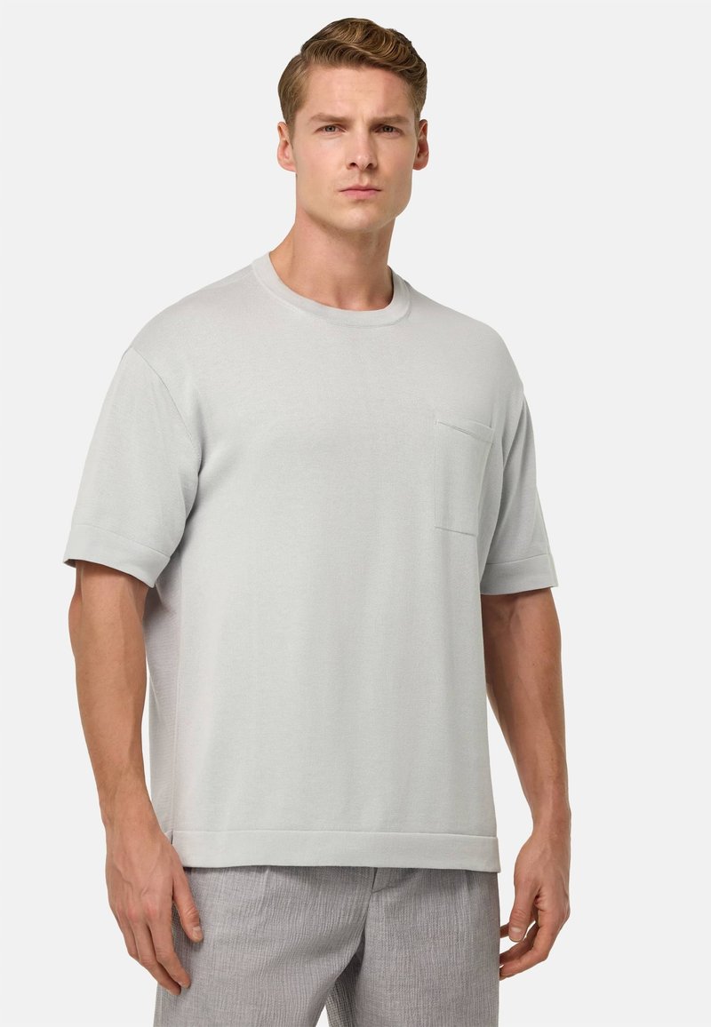 T-shirt di cotone grigio chiaro con colletto rotondo, maniche corte e taschino frontale. Presenta una vestibilità rilassata e una texture liscia.